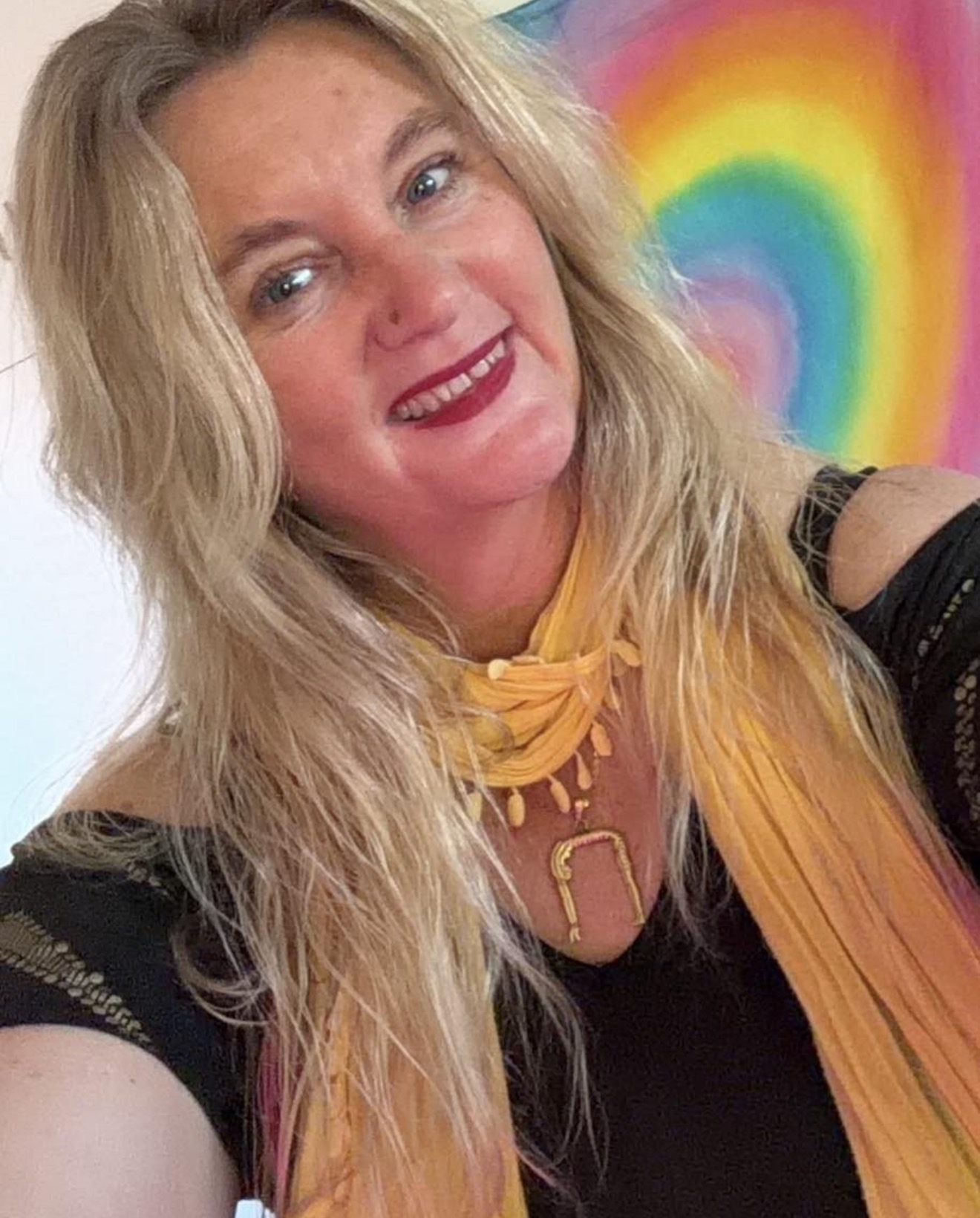 Mystic Nic smiling with a rainbow artwork behind her