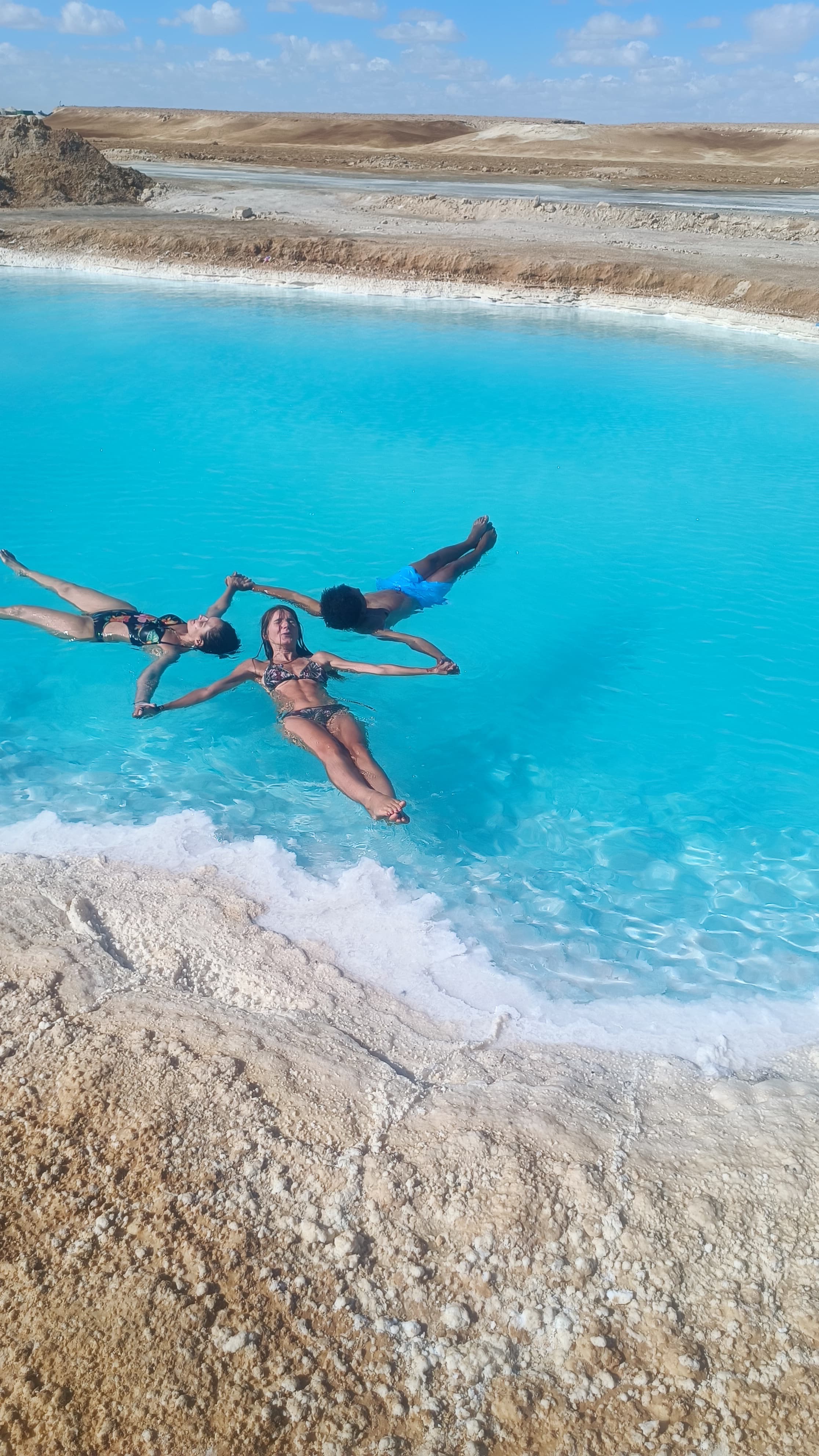 Three people floating in the turquoise Siwa Salt Lakes
